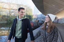 Felice giovane coppia che si tiene per mano, passeggiando lungo il canale urbano — Foto stock