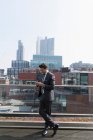 Homme d'affaires utilisant un téléphone intelligent sur un balcon ensoleillé et urbain — Photo de stock