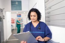 Женщина-врач с медицинской картой делает обходы в коридоре больницы — стоковое фото