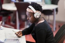 Studentin mit Kopfhörer mit Smartphone im Klassenzimmer — Stockfoto