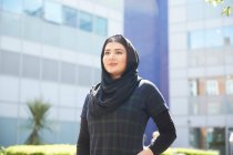 Retrato confiado joven mujer usando hijab fuera soleado edificio - foto de stock