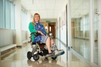 Mujer sonriente retrato con bota médica en silla de ruedas en pasillo - foto de stock