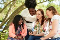 Female friends using smart phone in park — Stock Photo