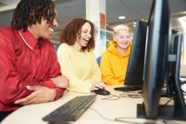 Счастливые студенты колледжей вместе учатся за компьютером в библиотеке — стоковое фото