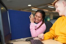 Happy young female college students laughing at computer in library — Stock Photo
