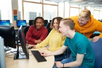 Счастливые молодые студенты колледжа вместе пользуются компьютером в библиотеке — стоковое фото