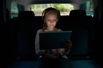 Fille avec écouteurs et tablette numérique sur le siège arrière de la voiture — Photo de stock