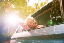 Carefree girl reaching arm out sunny car window — Stock Photo