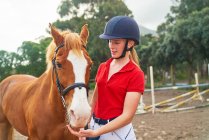 Adolescente no capacete equestre com cavalo no paddock — Fotografia de Stock
