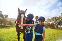 Happy girls petting horse in sunny rural paddock — Stock Photo