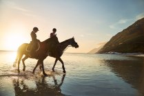 Young women horseback riding in sunny sunset ocean surf — Stock Photo