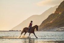 Mujer joven galopando a caballo en el océano tranquilo surf - foto de stock