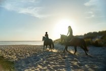 Young women horseback riding on sunny idyllic ocean beach — Stock Photo