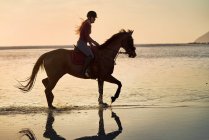 Jeune femme équitation dans le coucher du soleil océan surf — Photo de stock