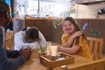 Счастливая молодая женщина с синдромом Дауна смеется с друзьями в кафе — стоковое фото