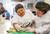 Des jeunes femmes souriantes atteintes du syndrome de Down coupant des pommes de terre dans la cuisine — Photo de stock
