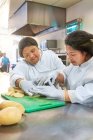 Mujeres jóvenes con síndrome de Down cortar patatas en la cocina cafetería - foto de stock