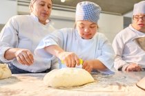 Jeune femme avec le syndrome de Down couper la pâte dans la classe de cuisson — Photo de stock