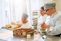 Chef y estudiantes con síndrome de Down horneando pan en la cocina - foto de stock