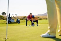 Male golfers planning putt on sunny golf greens — Stock Photo