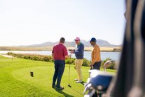 Чоловіки гольфи розмовляють на коробці трійника на сонячному полі для гольфу — стокове фото