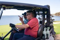 Los golfistas masculinos que conducen carro del golf en campo de golf del lago - foto de stock
