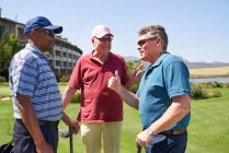 Счастливые друзья-гольфисты разговаривают на солнечном поле для гольфа — стоковое фото