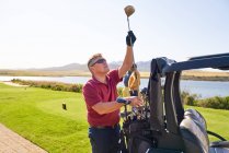 Golfista masculino escolhendo clube de golfe no tee box no campo de golfe ensolarado — Fotografia de Stock