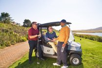 Hombres amigos golfistas hablando en el soleado carrito de golf - foto de stock