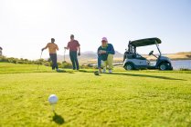 Male golfers preparing to tee off at sunny tee box — Stock Photo