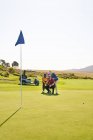 Masculino golfistas planejamento putt tiro no ensolarado campo de golfe colocando verde — Fotografia de Stock