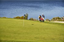 Male golfers planning putt shot at sunny lakeside golf course — Stock Photo