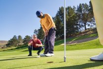 Чоловік гольф кладе в отвір на сонячному полі для гольфу, ставлячи зелений — стокове фото