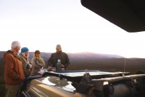 Safari guía turístico y grupo disfrutando de café fuera del vehículo todoterreno - foto de stock