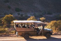 Сафарі екскурсовод і група в позашляховому транспорті на сонячній брудній дорозі — стокове фото