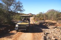 Safari tour grupo montando em veículo off-road na estrada de terra ensolarada — Fotografia de Stock