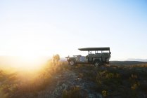 Safari tour grupo fuera del vehículo todoterreno en una colina tranquila al amanecer - foto de stock