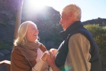 Счастливая пожилая пара, держащаяся за руки на солнечном балконе — стоковое фото