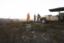 Safari tour group drinking tea outside off-road vehicle at sunrise — Stock Photo
