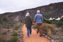 Senior couple holding hands on footpath outside safari lodge cabins — Stock Photo