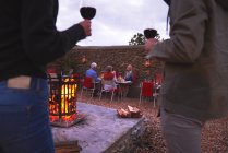 Casal e amigos seniores jantando beber vinho no pátio com fogueira — Fotografia de Stock