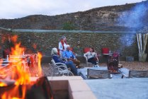 Amigos seniores relaxando com vinho tinto no pátio do hotel com fogueira — Fotografia de Stock