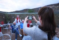 Femme avec appareil photo téléphone photographier des amis âgés sur le patio de l'hôtel — Photo de stock