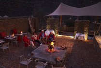 Amigos mayores que se relajan con el vino en el fuego en el patio del hotel - foto de stock