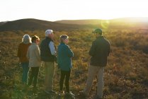 Safari guía turístico hablando con el grupo en los pastizales soleados de Sudáfrica - foto de stock