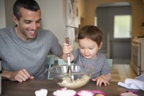 Счастливый отец и дочь малыша пекут за кухонным столом — стоковое фото