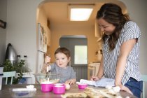 Mother and cute toddler daughter baking at kitchen table — Stock Photo