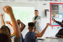 High school teacher leading lesson, calling on students with arms raised in classroom — Stock Photo