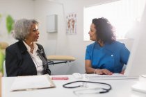 Female doctor talking with senior patient at computer in doctors office — Stock Photo