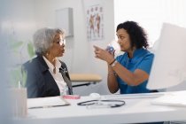 Женщина-врач учит пожилого пациента, как использовать ингалятор в офисе врача — стоковое фото